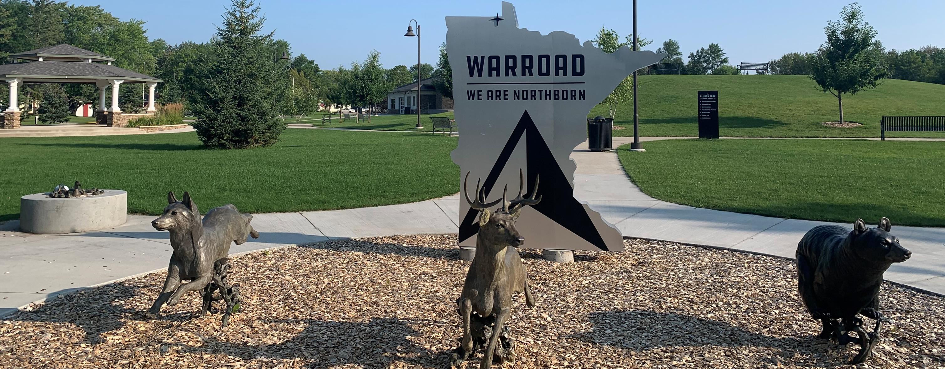 Minnesota shaped sign saying We are northborn sign in park with three animal statue in front of sign